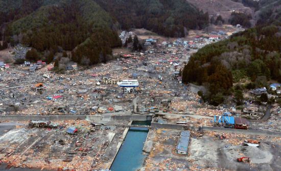 Aerial photo of devastated Japanese village. In the center of the picture is a boat on top of a house.